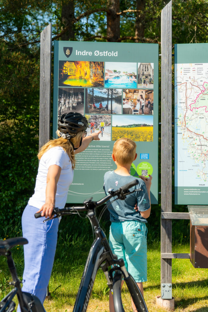 Kvinne og gutt på sykkel som ser på et kart over Indre østfold. Foto av Jonas Ingstad / Visit Indre Østfold. 